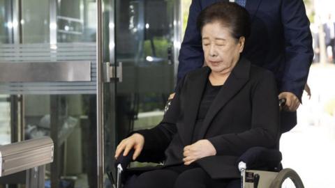 Unification Church leader Han Hak-ja, dressed in a black coat and seated on a wheelchair, arrives for an arrest warrant hearing on allegations of bribery and political funding, at the Seoul Central District Court in Seoul