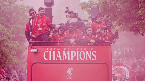Liverpool players celebrate on an open-top bus, as a red flare colours the throngs of fans around it