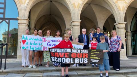 Group of parents and children standing on the steps outside the Guildhall in Northampton holding banners.