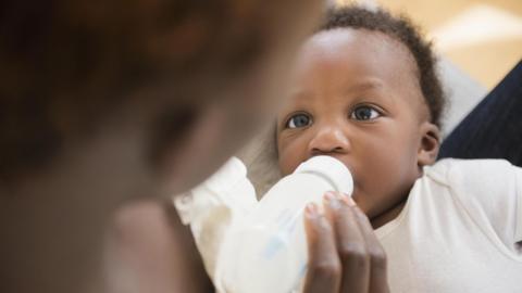 A close up of a baby being fed from a bottle by its mother