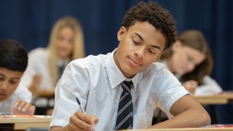 A young schoolboy with short brown hair wearing a white shirt and black striped tie.
