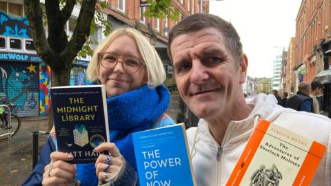 Man and woman hold books on street.