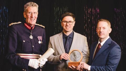 Left to right David Fursdon, His Majesty’s Lord-Lieutenant of Devon, Luminous founders Edwin Samkin and Mike Badley at the awards. The co-founders are holding a trophy. 