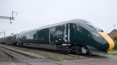 A green GWR train with a yellow front panel travelling on rail tracks