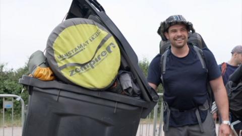 Man standing with wheelie bin full of camping equipment