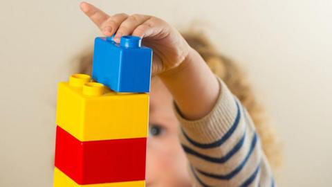 Generic image of a pre-school child making red yellow and blue building blocks into a tower