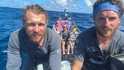 Three brothers sitting in a large rowing boat on the ocean.