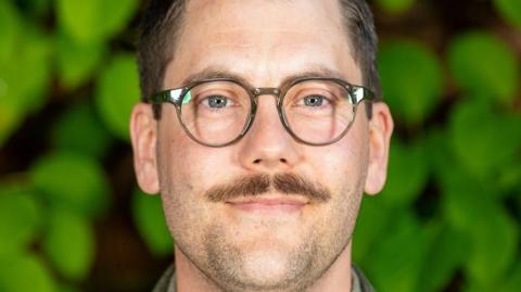 A man with a moustache and glasses is smiling