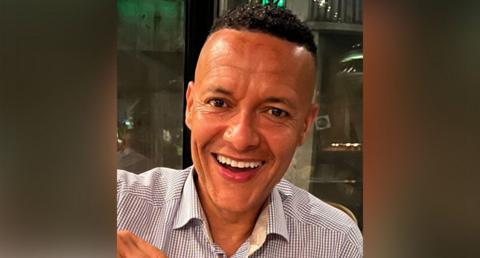 Clive Lewis smiling at the camera while wearing a shirt 