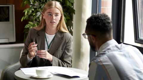 A young woman sits in an office area during an interview