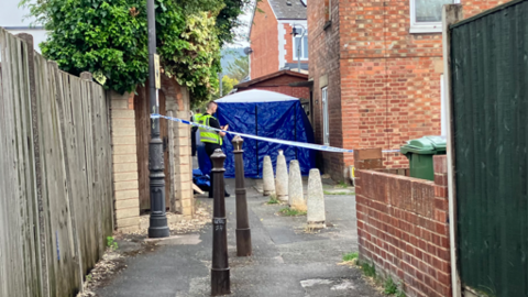 An alleyway with a police cordon and blue tent at the end of it