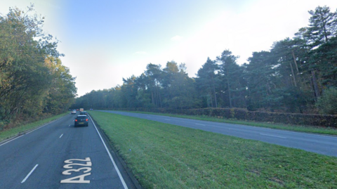 A Google street view screenshot of a four-lane road with a large grass verge in the middle separating the two carriageways. There are trees on either side.