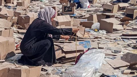 A woman pictured picking through broken cardboard boxes on the ground