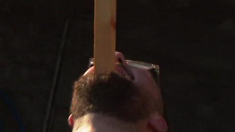 Man balancing plank of wood on his face