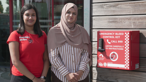 Sienna Ahir, Member of Youth Parliament and founder of Daggers Down, and councillor Obaida Ahmed stand by one of the kits at WV Active Bilston-Bert Williams.  Sienna has a red t-shirt on with Daggers Down on it and Obaida has a headscarf on over a striped shirt.


