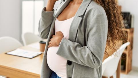 A woman is pregnant and talking on a smartphone while working at an office.