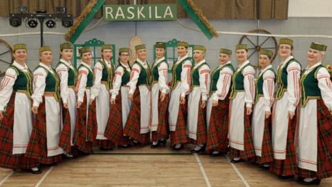 Dancers dressed in traditional Lithuanian attire - red checked skirts and white aprons with green vests and green headgear