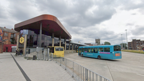 A street view image of the outside of the Wigan interchange bus station. There are two buses parked outside.
