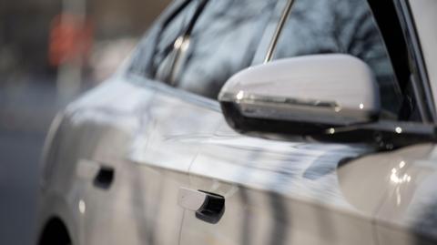 Close-up of a light coloured car. Car door handles are seen with a wing mirror and windows.