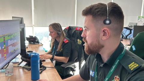 Inside the control room at the North East Ambulance service. Staff are wearing headsets and taking 99 calls. They are working on computers.