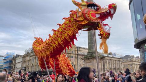 Hundreds of people are next to Grey's Monument in Newcastle with an orange dragon held in the air 