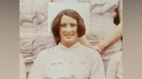 A historic sepia photograph of a female nurse in white uniform smiling at the camera.