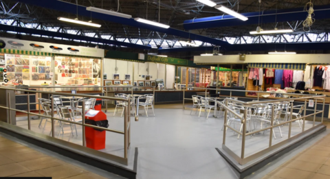 The inside of Bridgend market with stalls in background and a seating area at front with meta chairs and tables