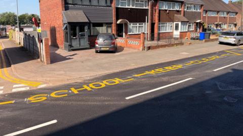A street with a sign painted in yellow that reads School - Keep - Clear.