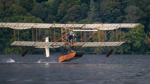 Waterbird, a bamboo seaplane, gliding on the water at Windermere. Trees can be seen in the background.