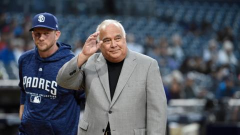 Ron Fowler, executive chairman of the San Diego Padres and prospective chairman of Lincoln City, waves while wearing grey suit over black top, as he stands alongside San Diego Padres manager Andy Green, who is wearing team-branded leisurewear