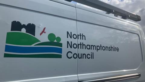 A white van which is parked. It has the words "North Northamptonshire Council" printed, and a green and blue council logo beside it.