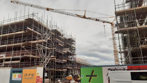 Two block of flats are covered in scaffolding as they are being built in Sunniside, Sunderland. The site is fenced off with a tall yellow crane towering above the buildings. 