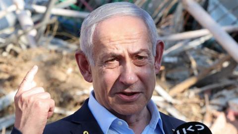 Benjamin Netanyahu speaks in front of a pile of rubble.