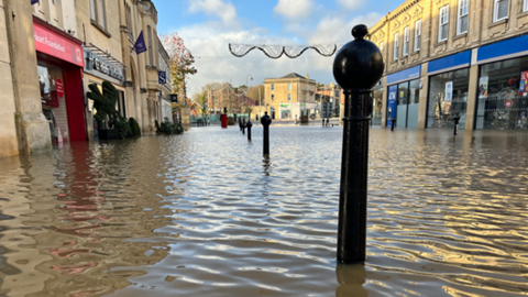 flooding through the high street, with water lapping against the front of business premises - bollards in foreground 