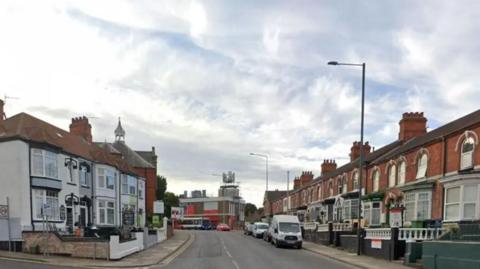 Isaac's Hill in Cleethorpes showing a road with houses on either side. A white van is parked on the right hand side of the road and behind it are four cars and a bus. 