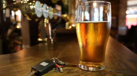 A set of keys sitting next to a mostly full pint glass