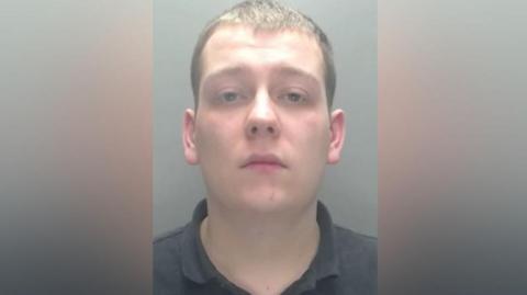 Mugshot of Thomas English. He is clean-shaven with short dark hair and is wearing a black polo shirt