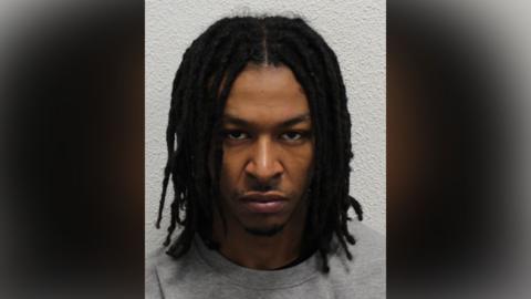 Police mugshot of Nathan Tokosi, wearing a grey sweatshirt and looking at the camera with a grumpy face.
