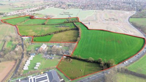 An elevated view of the proposed site highlighting seven green fields. Beside the fields is the A39.