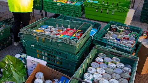 Boxes of tins stacked up outside. The green boxes contains hundreds of tins cans containing food.
