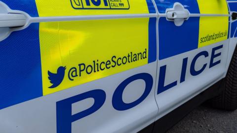 Close up of the side of a marked Police Scotland car, which includes the force's X handle and website in blue writing 