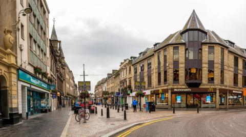 Looking down Inverness' pedestrianised High Street. Shops visible include a McDonalds and a Poundland. 