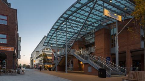 Exterior shot of Harlequin Theatre showing large glass covering and metal staircase leading up to entrance