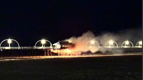 Smoke and fire billows from the pier surrounded by black sky