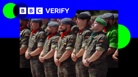 Spanish soldiers wearing differently-coloured berets stand in rows with their hands crossed in front of them. BBC Verify branding appears in the top left of the image.