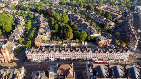 An aerial view of about 100 terraced houses on three different streets with some trees dotted about