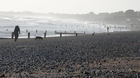 A rocky beach and sea shore. There is the silhouette of someone walking their dog. 