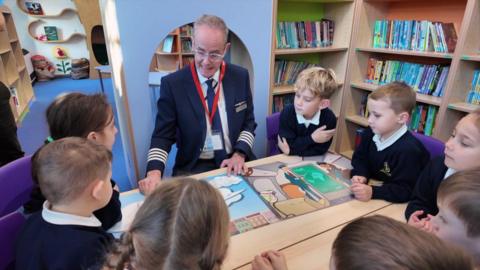 Airline pilot and author Rob Johnson reading his books among school children. The group appear to be in a school library.