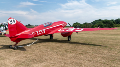 Red plane on a grass airfield. It has the number 34 painted on the tail fin.