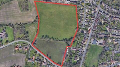 A bird's-eye view of the area that has been proposed for development. The space which is outlined in red currently is field space with several trees. 